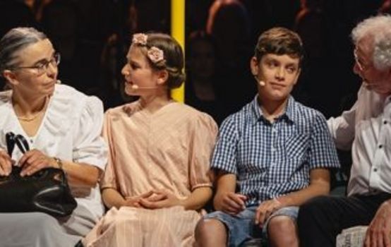 Eine ältere Dame und ein älterer herr sitzen auf einer Bank und unterhalten sich mit einem Mädchen und einem Jungen.