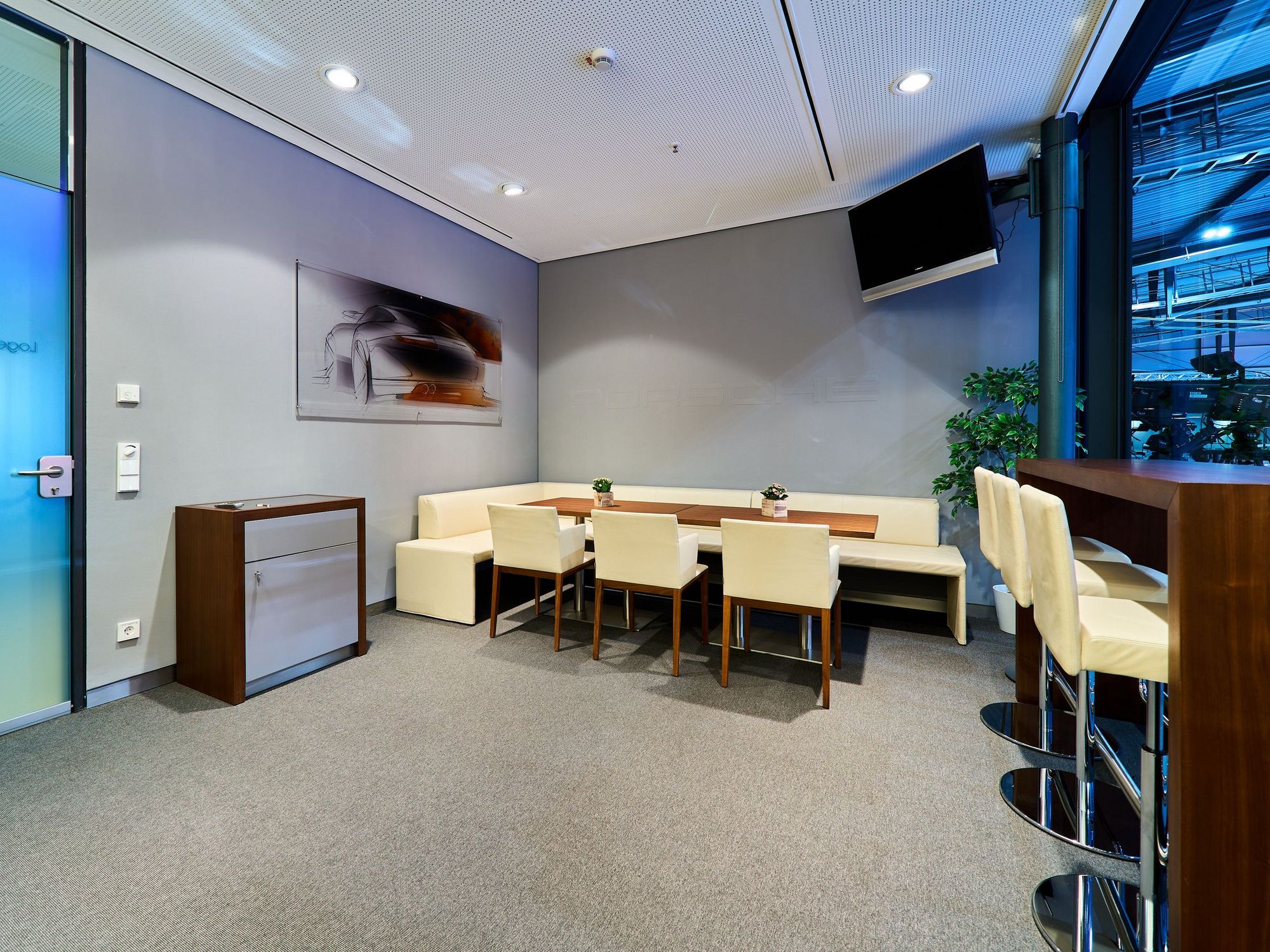 Blick in eine Loge der Porsche-Arena mit hochwertigen weißen Stühlen, einem langen Tisch und direktem Blick in die Arena  