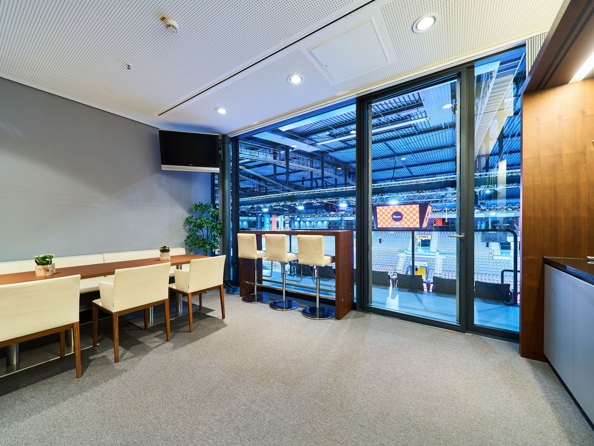 Blick in eine Loge mit weißen Stühlen, einem Bar-Tisch mit hohen Stühlen und direktem Blick in die Porsche-Arena