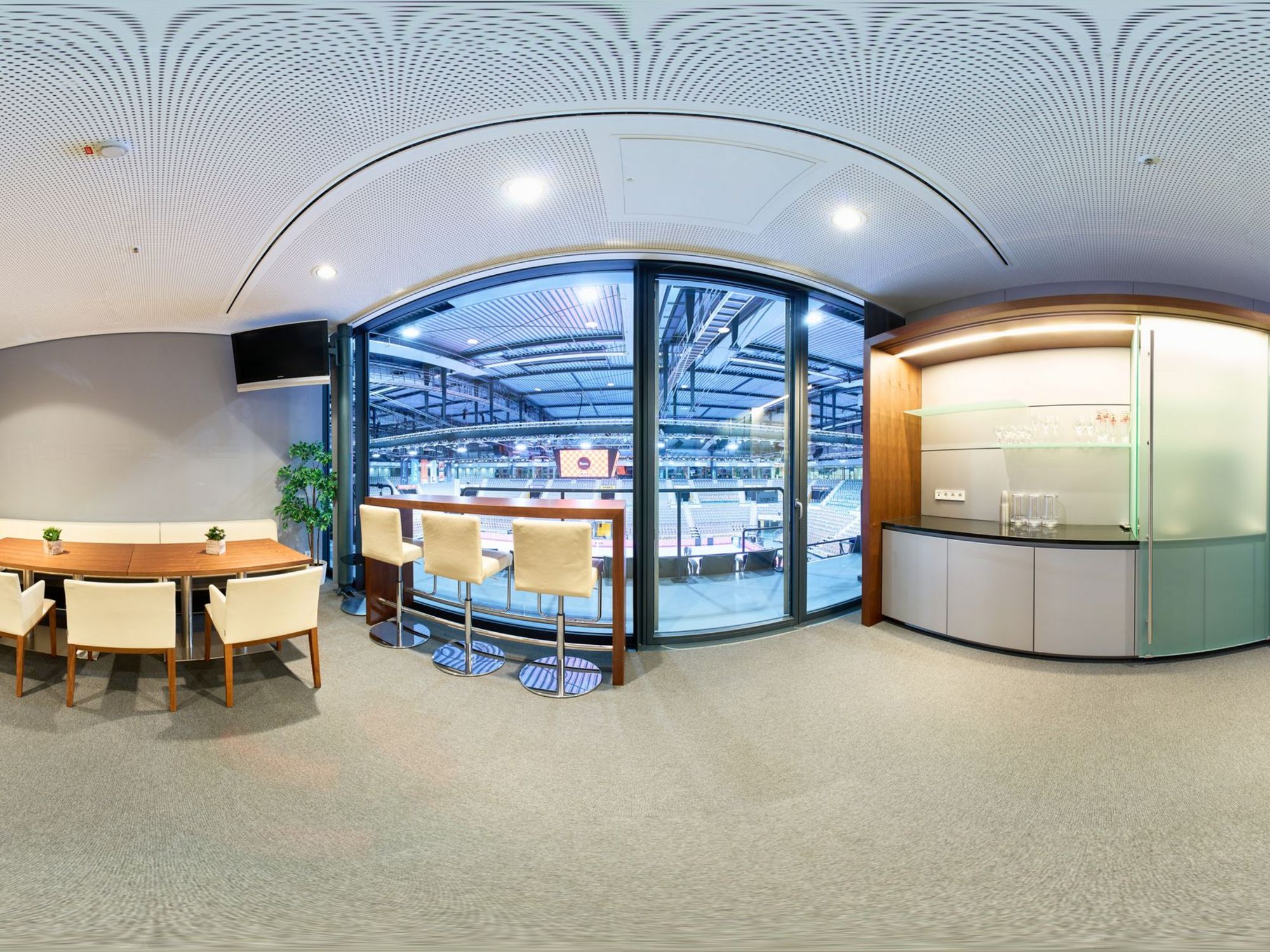 Panorama-Bild einer Loge mit weißen Sitzmöbeln, einem langen Tisch und einem Thresen.