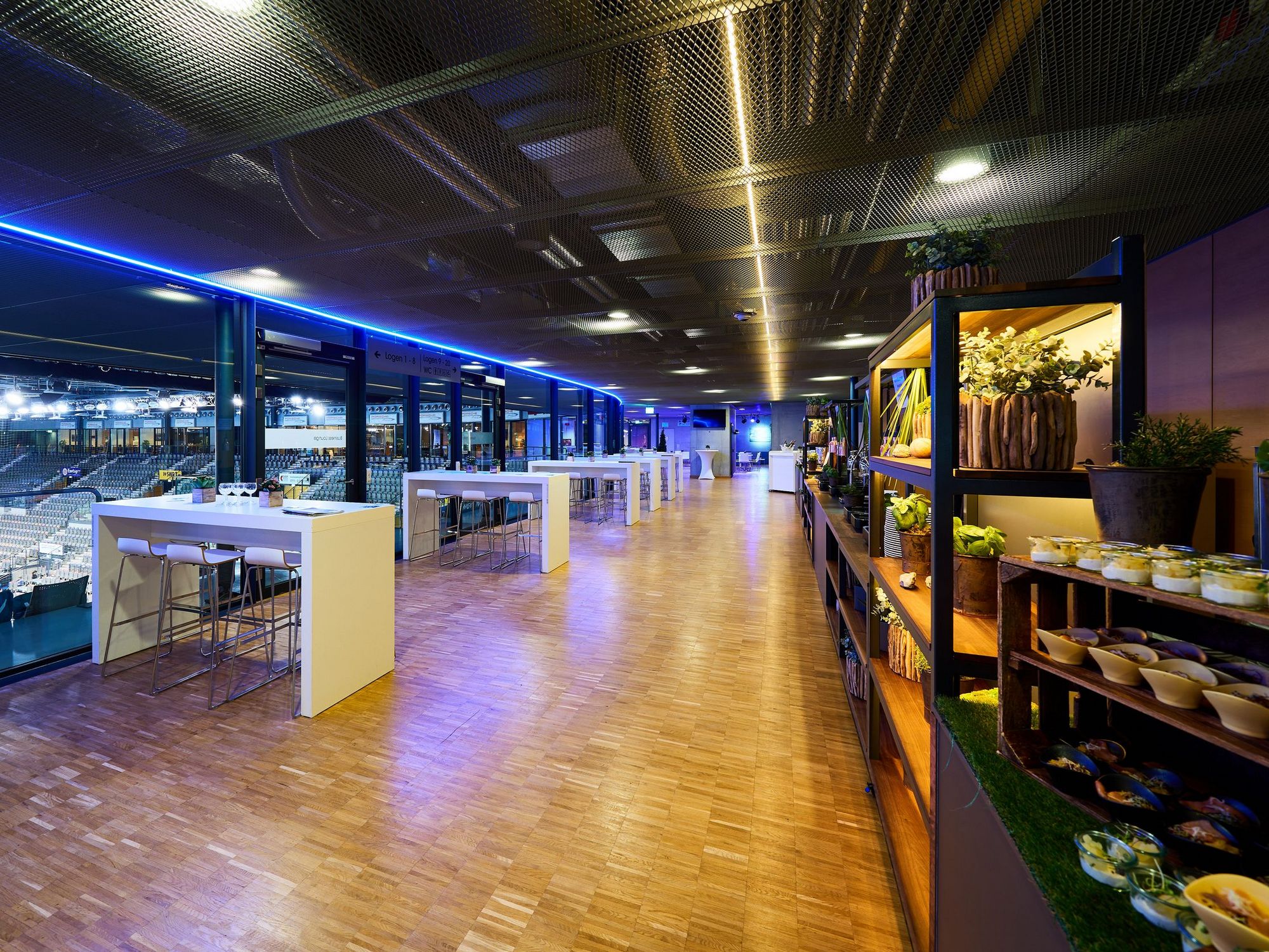 Stehtische mit direktem Blick in die Porsche-Arena auf der linken Seite. Rechts stehen Regale mit Essen vom Buffet.