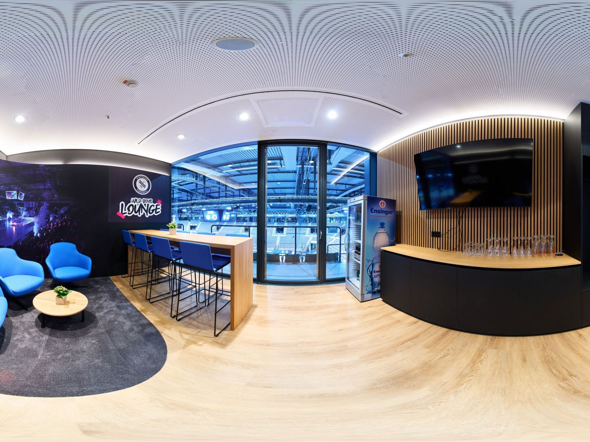 Panorama-Foto der Loge des TVB Stuttgart mit blauen Sitzmöbeln, einem kleinen runden Tisch, einem Thresen und dem Blick in die Porsche-Arena