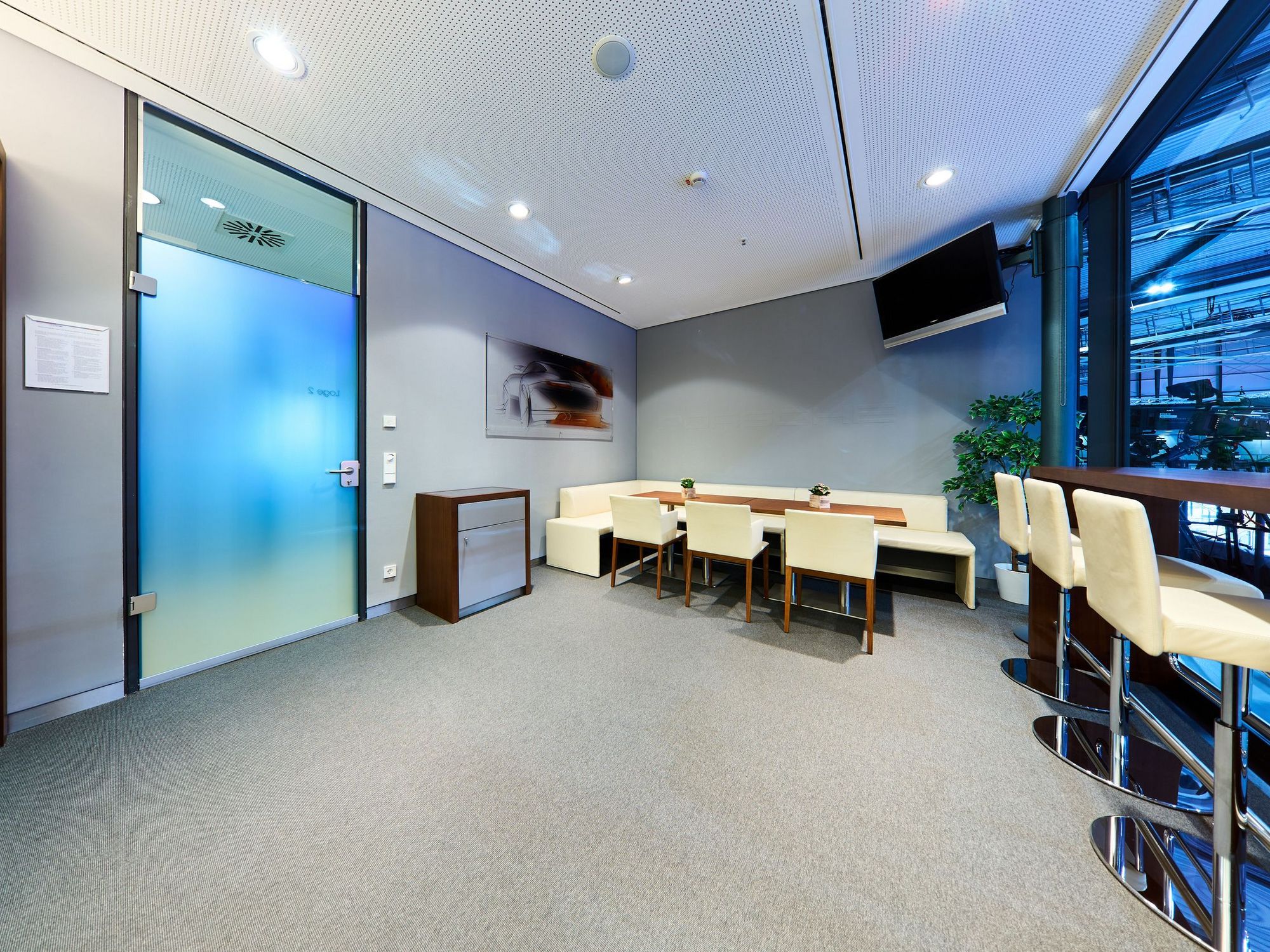 Blick in die Loge mit einem Kühlschrank, einer Sitzecke mit langem Tisch und einem Stehtisch mit Barhockern