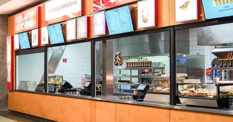 Ein oragefarbener Verkaufsstand im Hallenduo mit Getränke- und Essensangebot