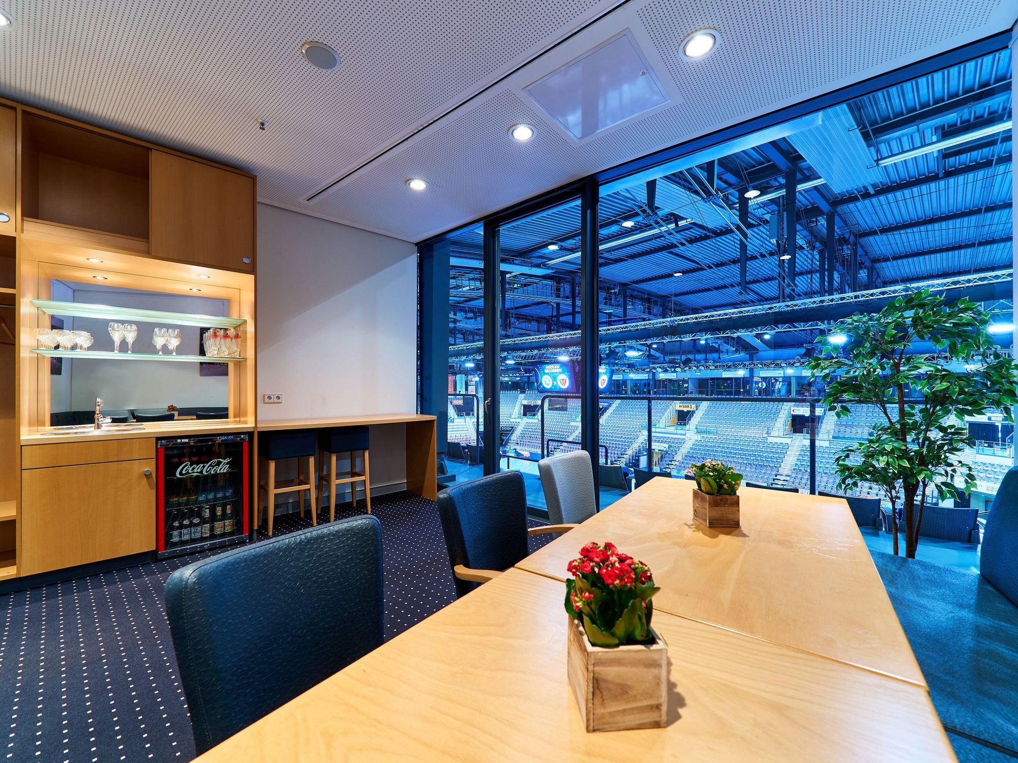 Eine Loge mit langem Holztisch, schwarzen Möbeln, einem Holzthresen und den direkten Blick in die Porsche-Arena
