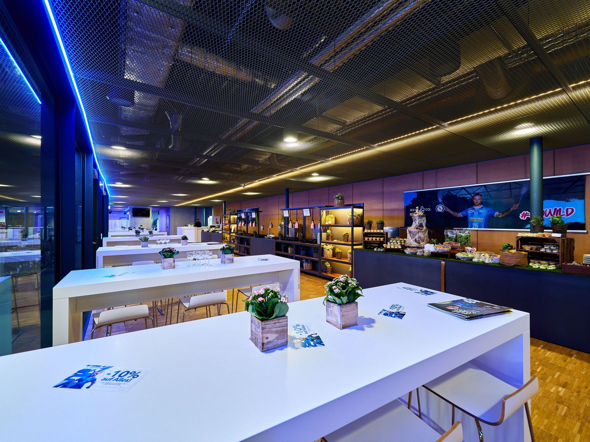 Weiße Stehtische mit Blick auf das aufgebaute Buffet im Hospitality-Bereich der Porsche-Arena