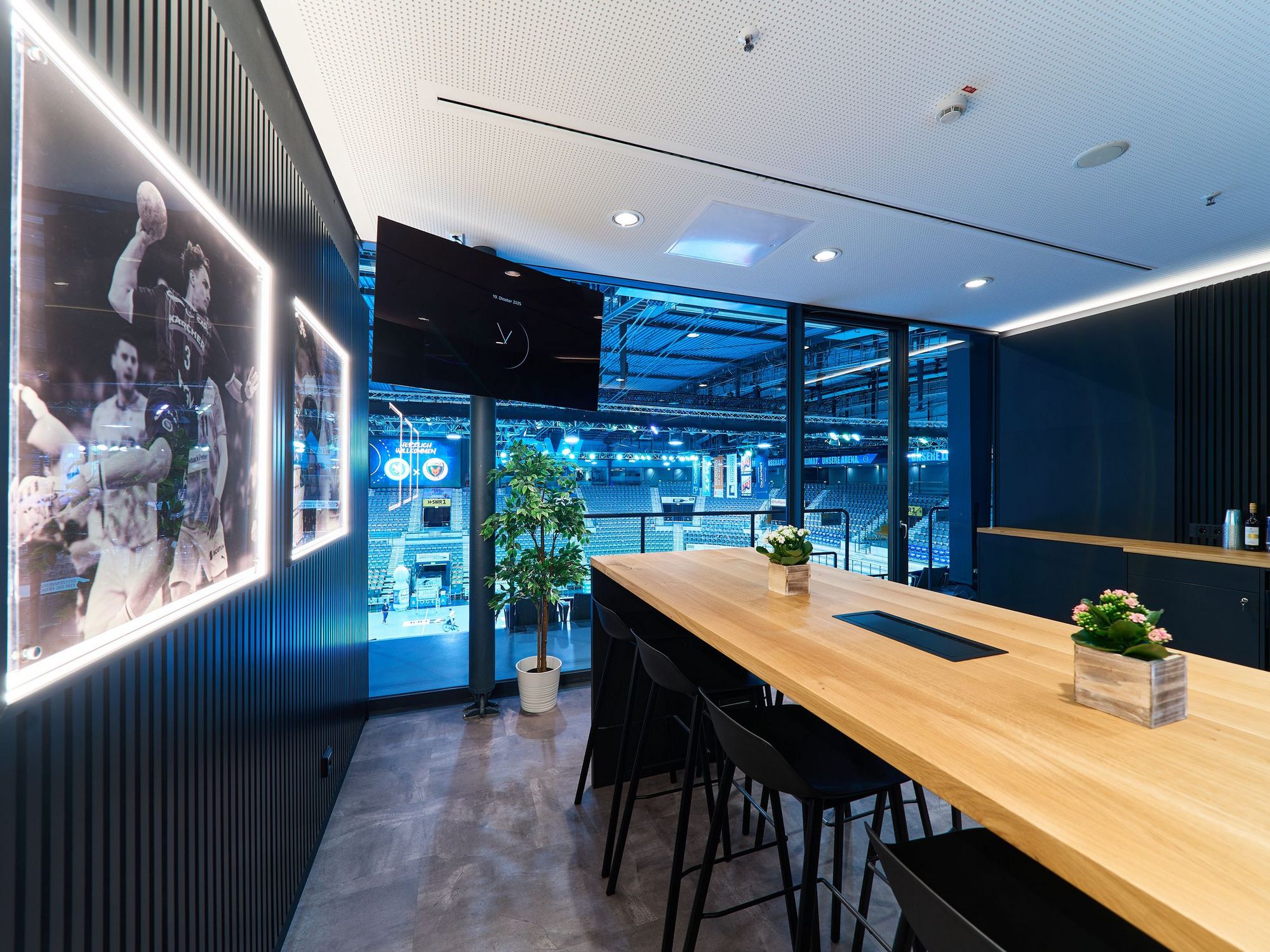 eine Loge mit langem Holztisch. An der Wand hängen Bilder vom Handball. 