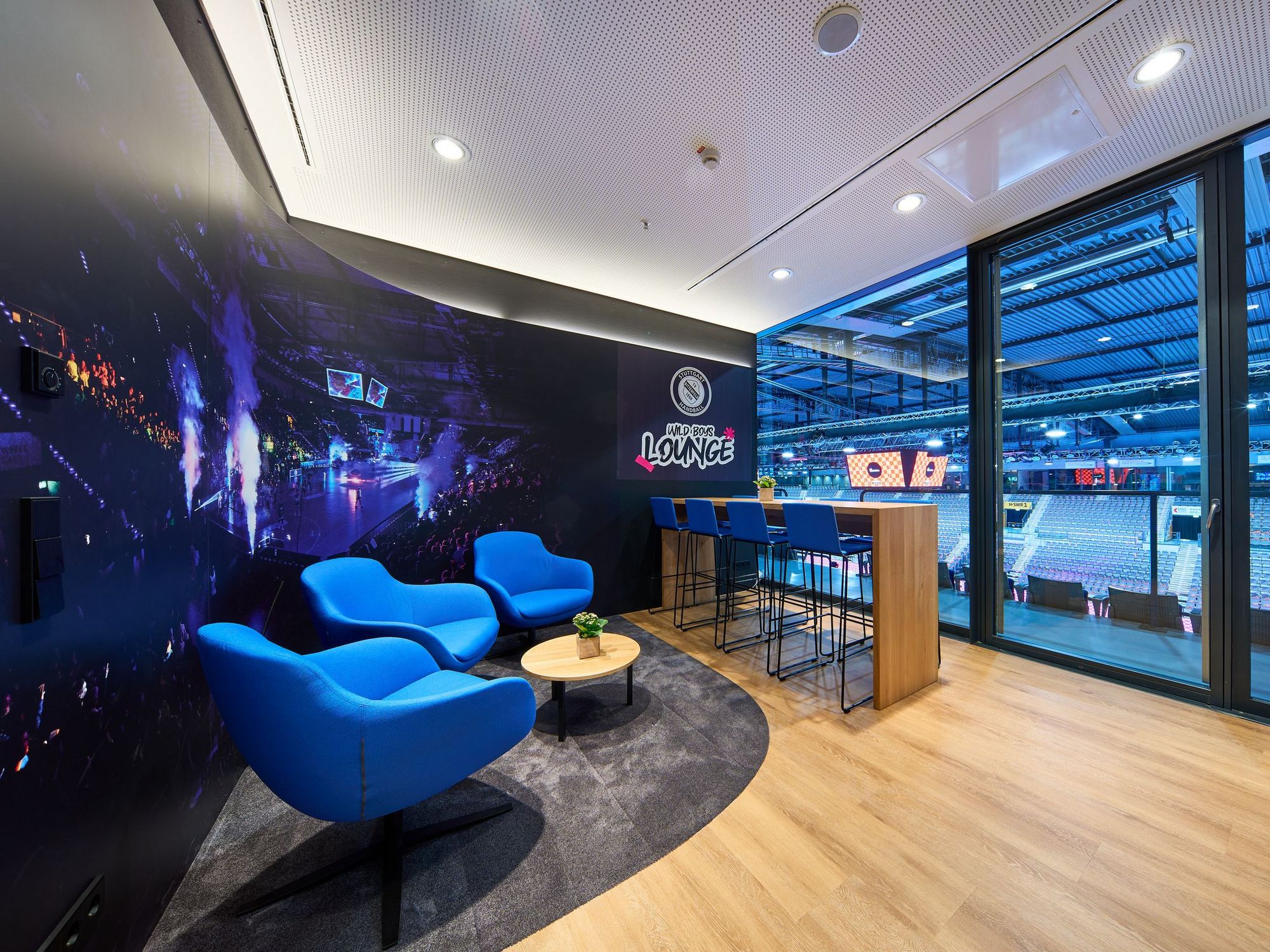 Die Loge des TVB Stuttgart mit blauen Sitzmöbeln, einem kleinen Couchtisch und einem Bartisch mit Barhockern.