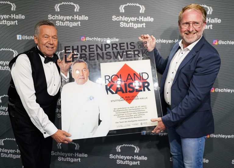 Roland Kaiser und René Otterbein halten den Ehrenpreis in Form einer Plexiglasplatte und lachen in die Kamera.