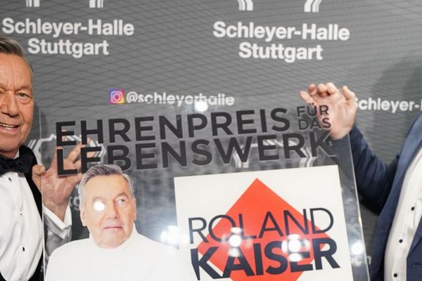 Roland Kaiser und René Otterbein halten den Ehrenpreis in Form einer Plexiglasplatte und lachen in die Kamera.
